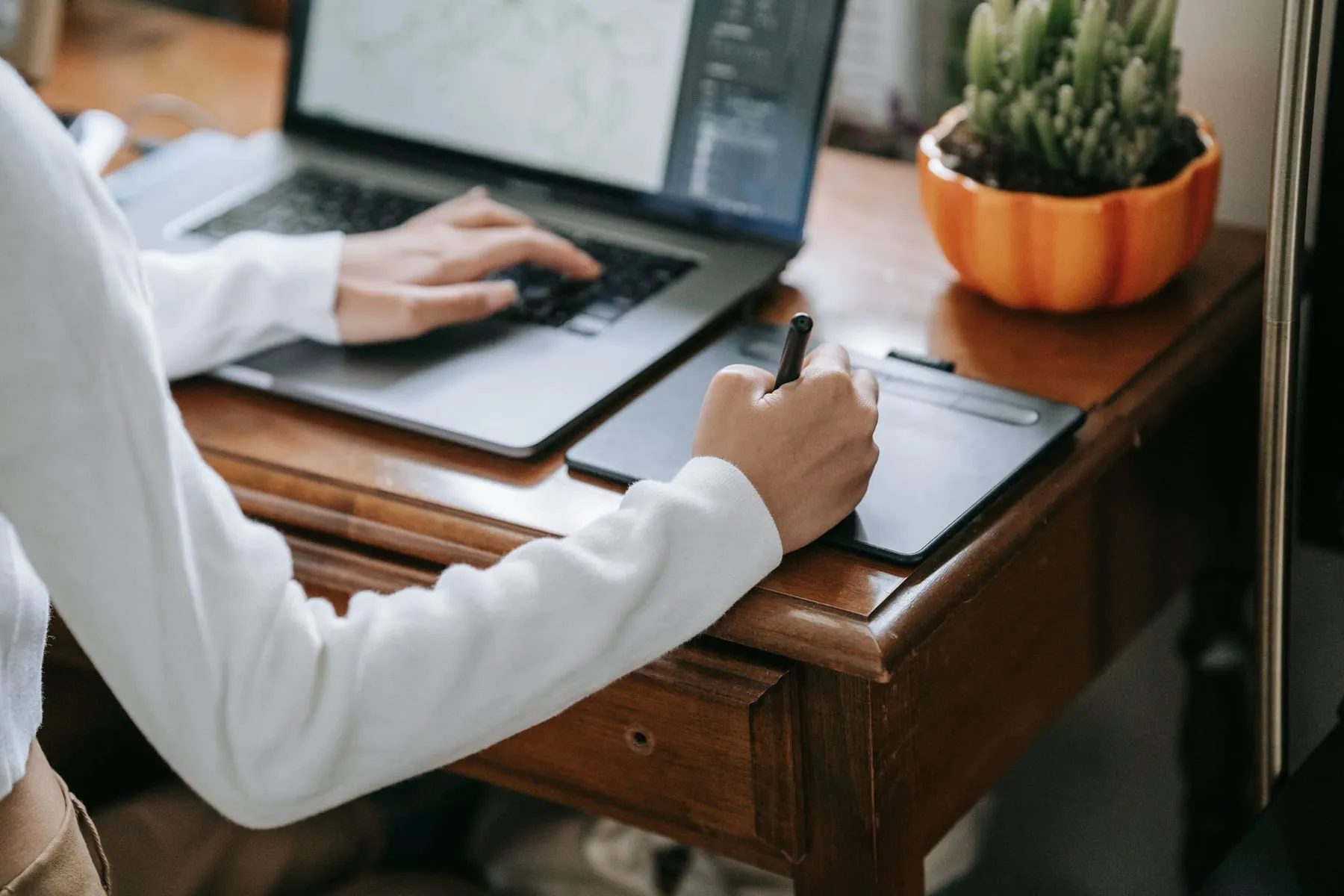 Designer desenhando em uma mesa digitalizadora ao lado do notebook